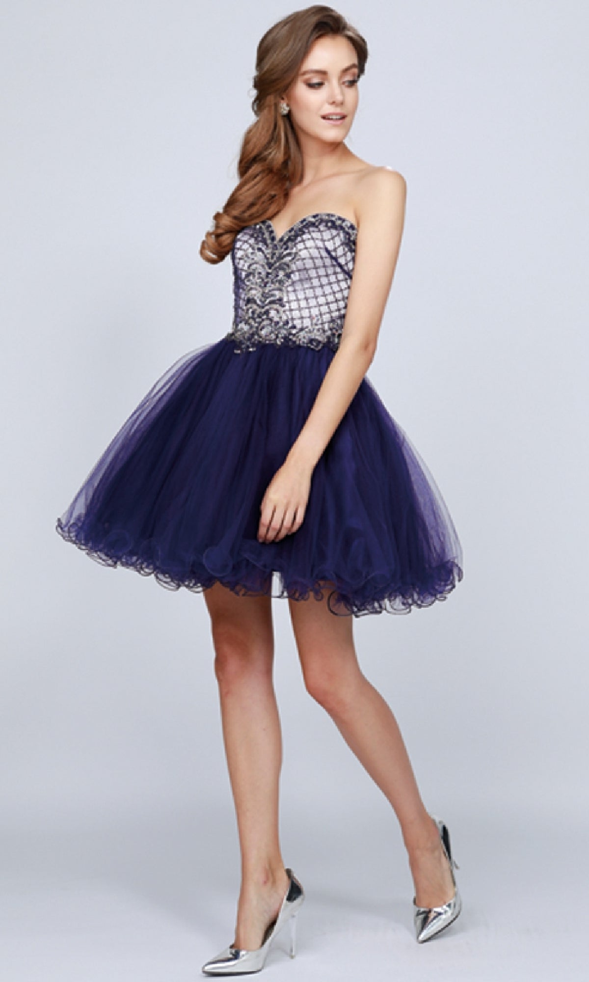 A woman wearing the Juliet 778 Short Babydoll Hoco Dress with a strapless sweetheart neckline, beaded bodice, dark tulle skirt, and paired with metallic silver heels.
